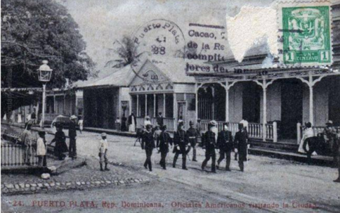c. 1916 to c. 1924: U.S. naval forces who captured and occupied Fortaleza de San Felipe at the start of the United States occupation of the Dominican Republic walk in the street on the northeast corner of area then known as Central Park (later Independence Square, now Parque Central Independencia (Independence Central Park). The psrk served as the center for social and political activity of Puerto Plata. City Hall, the Governor's Office, Catedral San Felipe Apóstol (St. Philip the Apostle Cathedral), The two males-only social clubs: (women could go there with their husbands) the Commerce Club and Faith in the Future Society all faced onto the park.